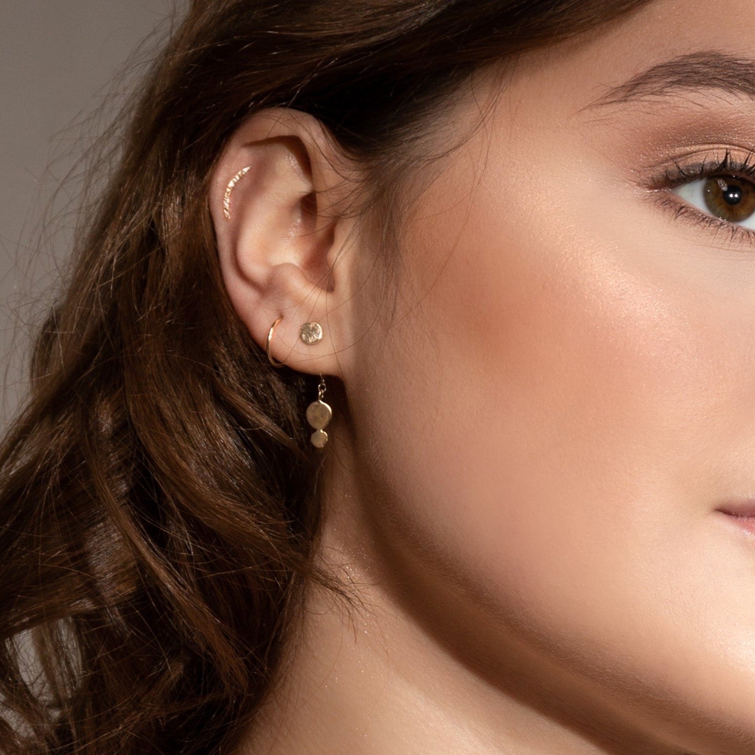 Solid 9ct gold crescent helix piercing earring worn alongside other olid gold earrings from the MUKA studio collection, all ethically handmade in UK