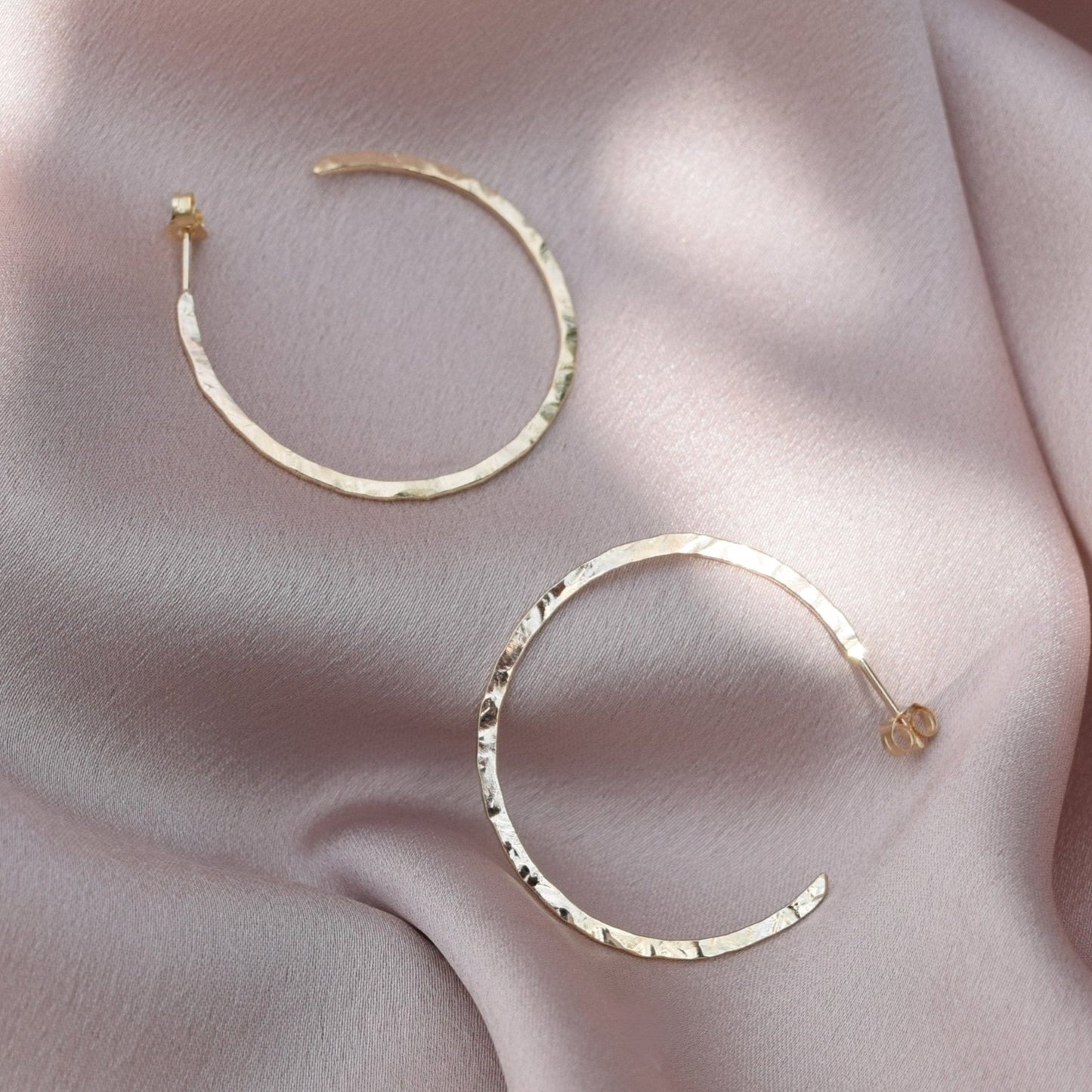 solid 9ct gold hoop earrings laying on a blush pink fabric background