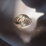 A stack of thin gold rings resting on a draped satin fabric under dramatic, directional sunlight and shadow.