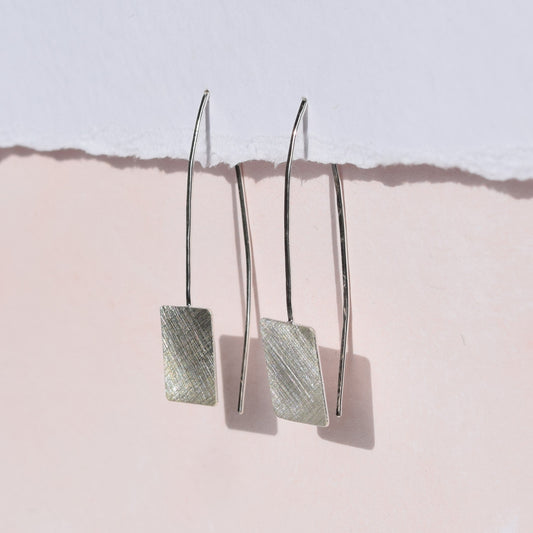 Square drop earrings on pink and white background