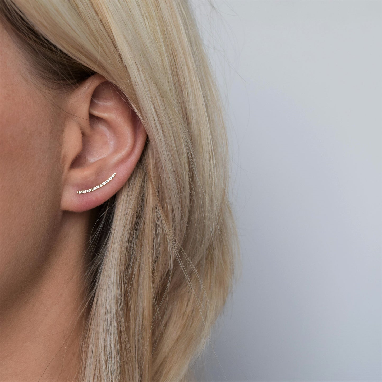 Gold ear climber with hammered finish worn by blonde haired model