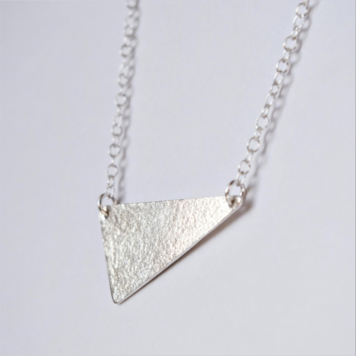 MUKA studio triangle necklace close up showing textured finish on silver pendant