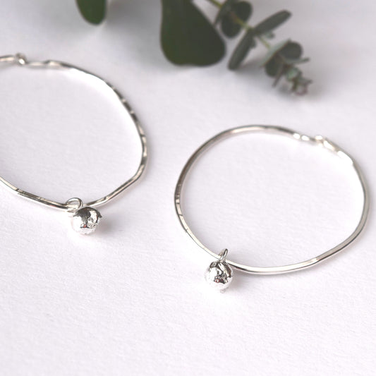 Silver oval hoop earrings with hanging silver ball worn by blond haired model