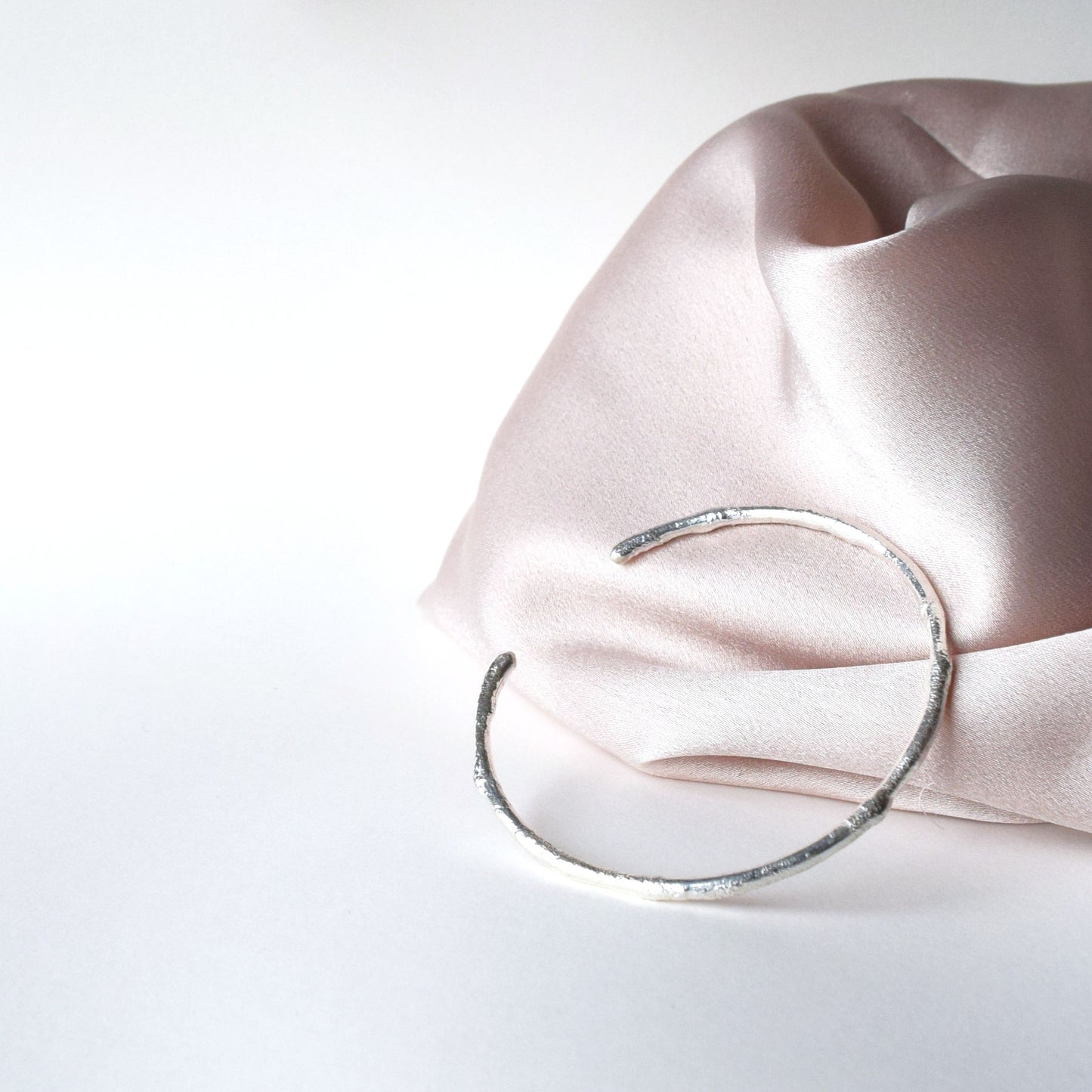 Product image of silver cuff with molten texture laying on pink satin fabric