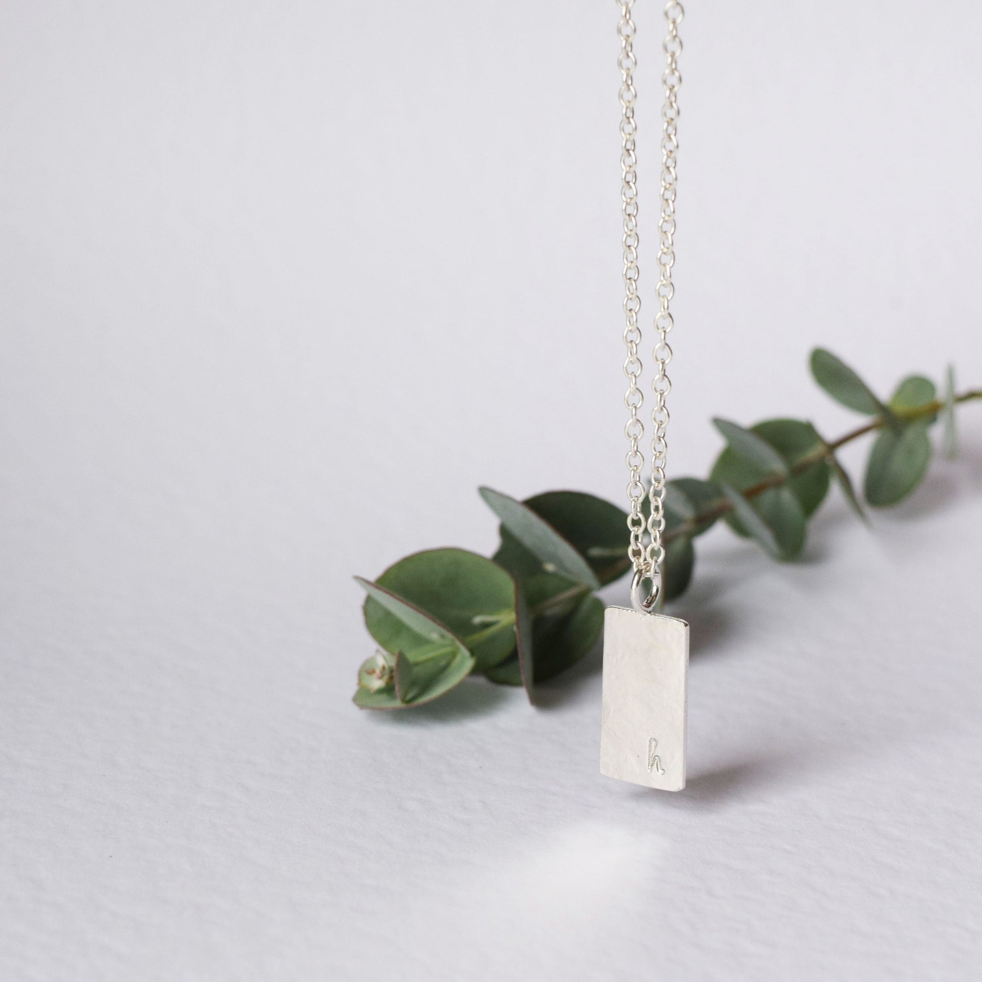 Personalised with the initial H this square pendant necklace is hanging with eucalyptus in the background