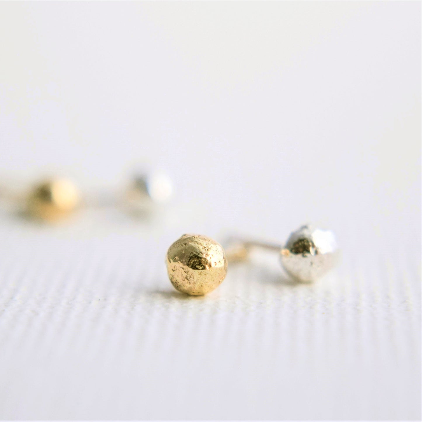 close up image of one gold and one silver organic ball stud showing the organic texture